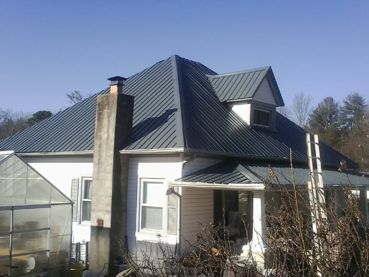 Dark blue standing seam metal roof on a white farmhouse with dormer — Slate & Tile Roof Repair by Roofing Brothers in Tustin